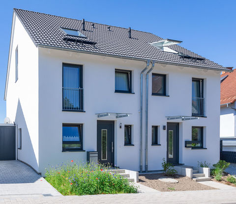 Ein weiß gestrichenes Doppelhaus mit Satteldach und angrenzender Garage.