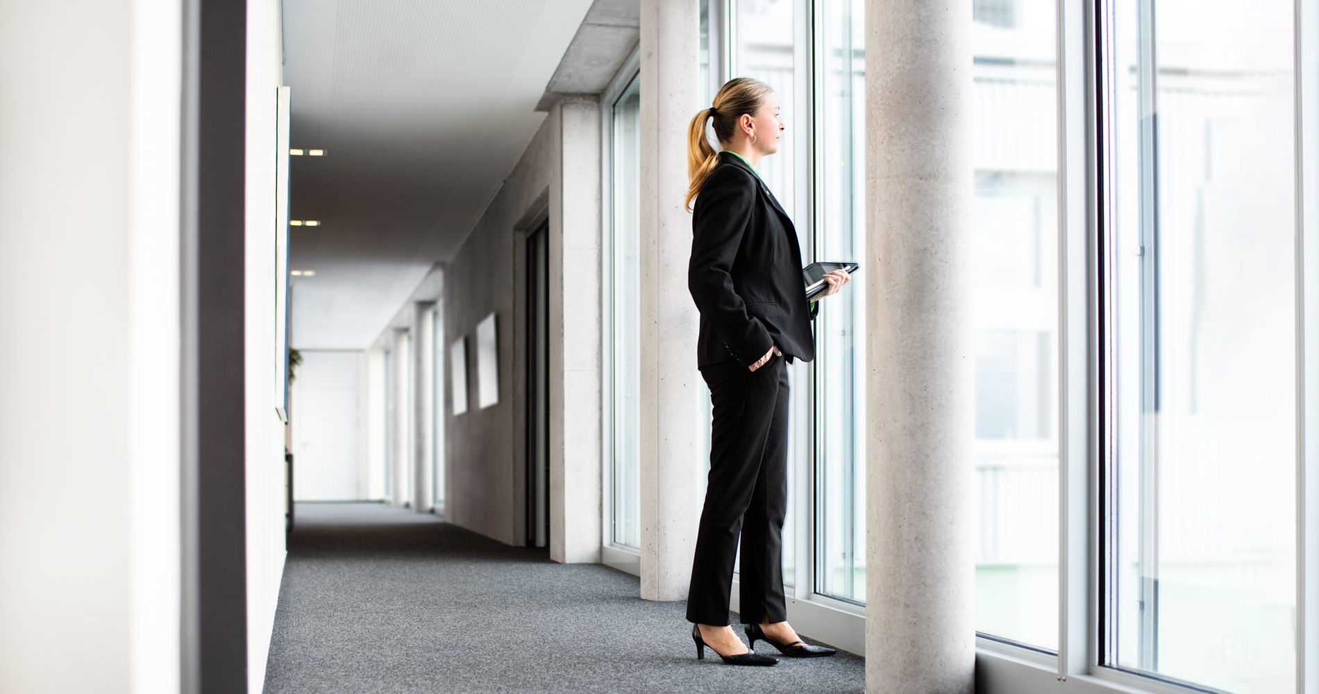 A woman in an office building looks out of the window into the distance