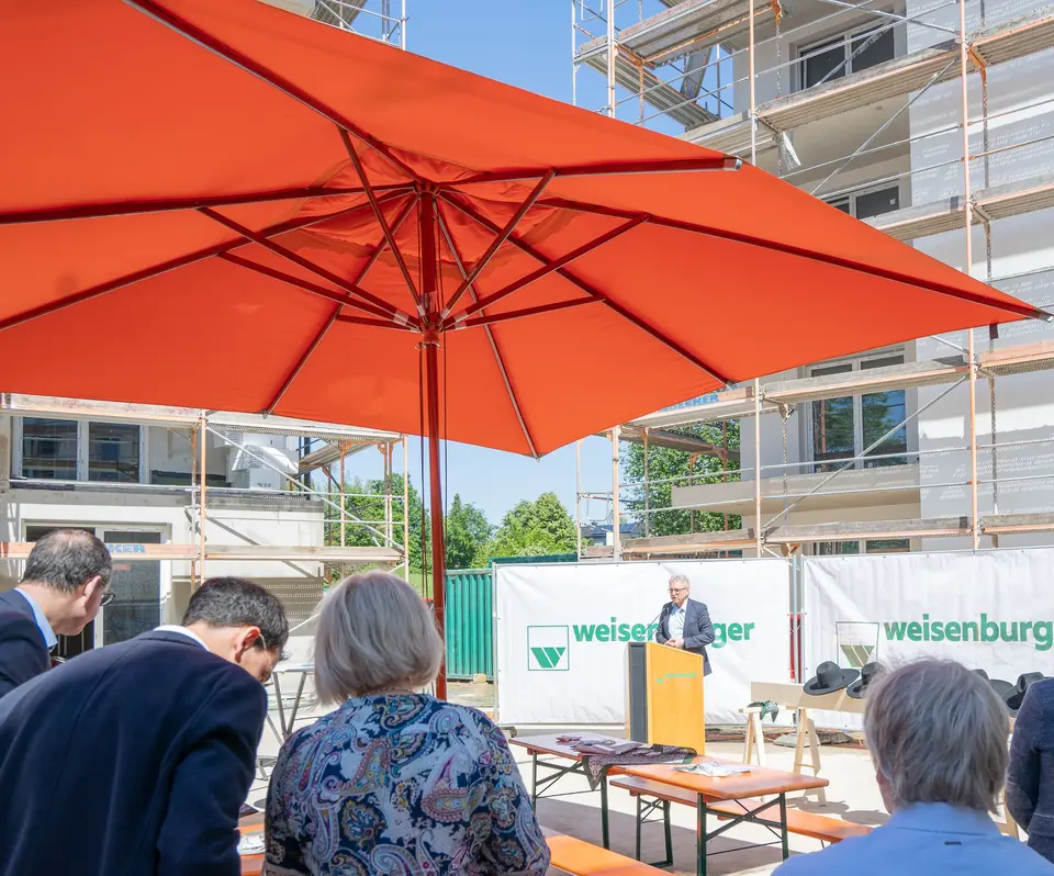 Personen stehen auf einer Baustelle und hören einem Mann zu welcher ein Vortrag hält