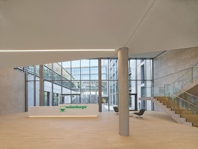 Foyer with reception counter, concrete column and an open staircase, with the inner courtyard of the building behind it.