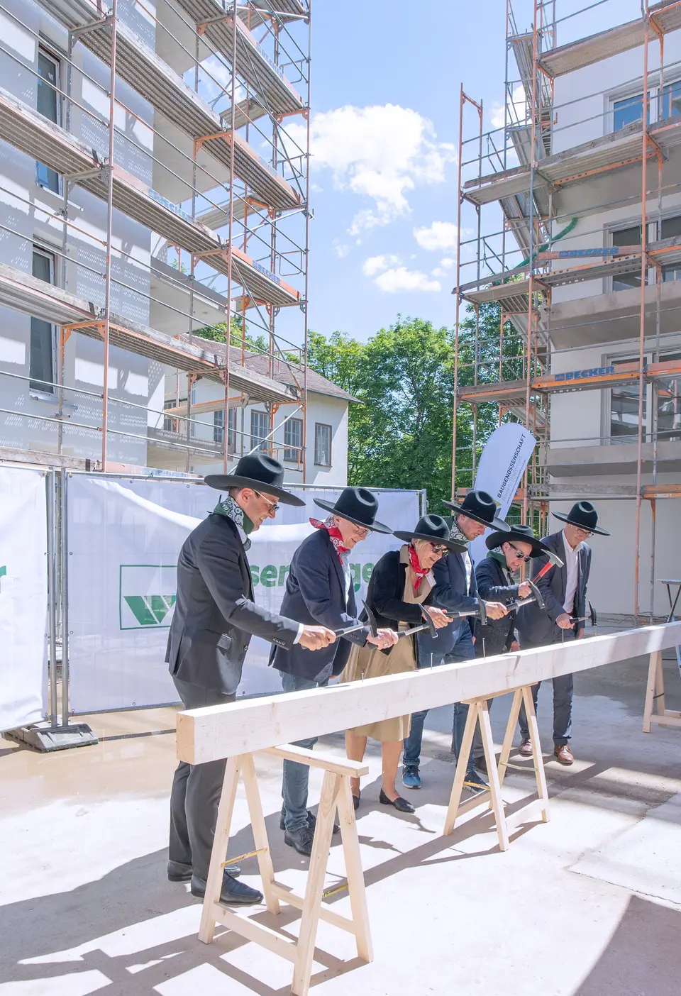 Fünf Männer und eine Frau hauen jeweils einen Nagel in einen Holzblock beim Richtfest