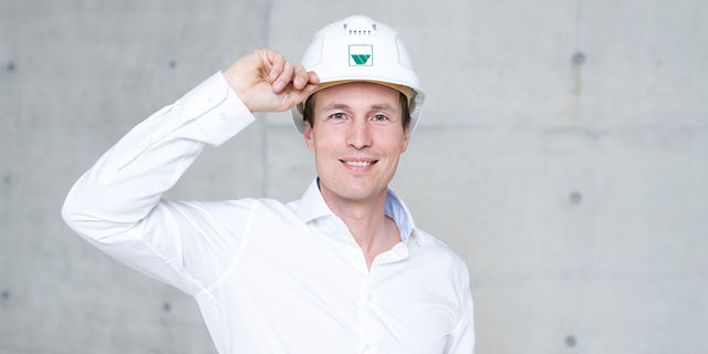 An employee in a white shirt grabs the white hardhat with his right hand
