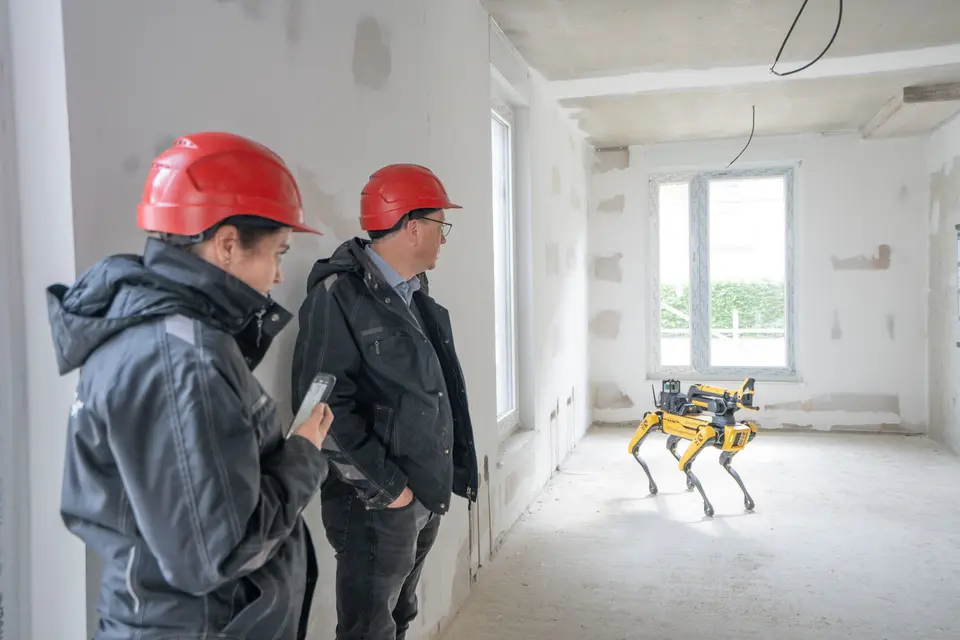 weisenburger Team mit Roboter auf Baustelle Zwei Männer mit rotem Bauhelm testen einen Boston Dynamics Spot Roboter auf einer Baustelle