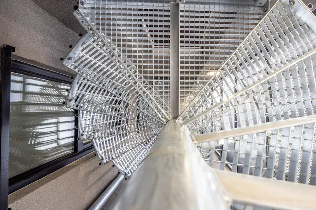 Metall-Wendeltreppe mit Gitter Eine silberfarbene Wendeltreppe aus Metall mit Gitterstufen im Innenraum. Blick von oben entlang der Spindel.