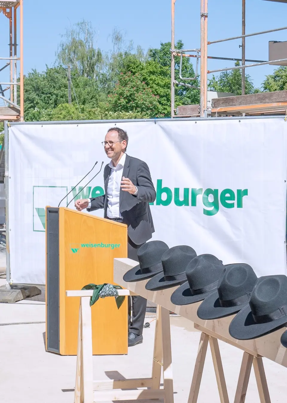 Eine Person hält eine Rede bei einem Richtfest vor einem Bauprojekt