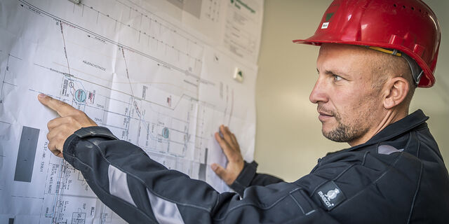 Planung-weisenburger-Bauleitung Mann mit Bauhelm schaut sich ein 2D Architekturplan an und zeigt auf diesen