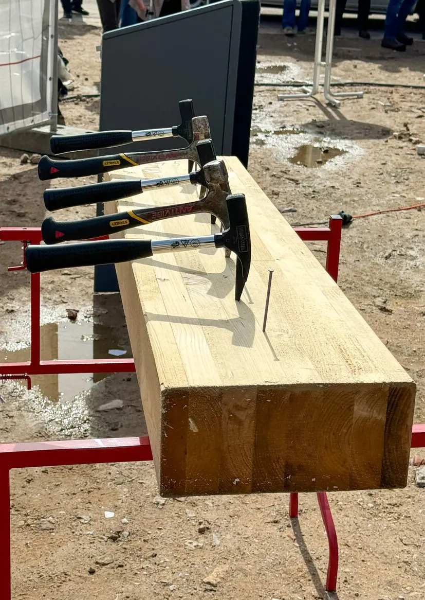 Hammer und Nagel stecken in einem Holzblock welcher auf einer Baustelle steht