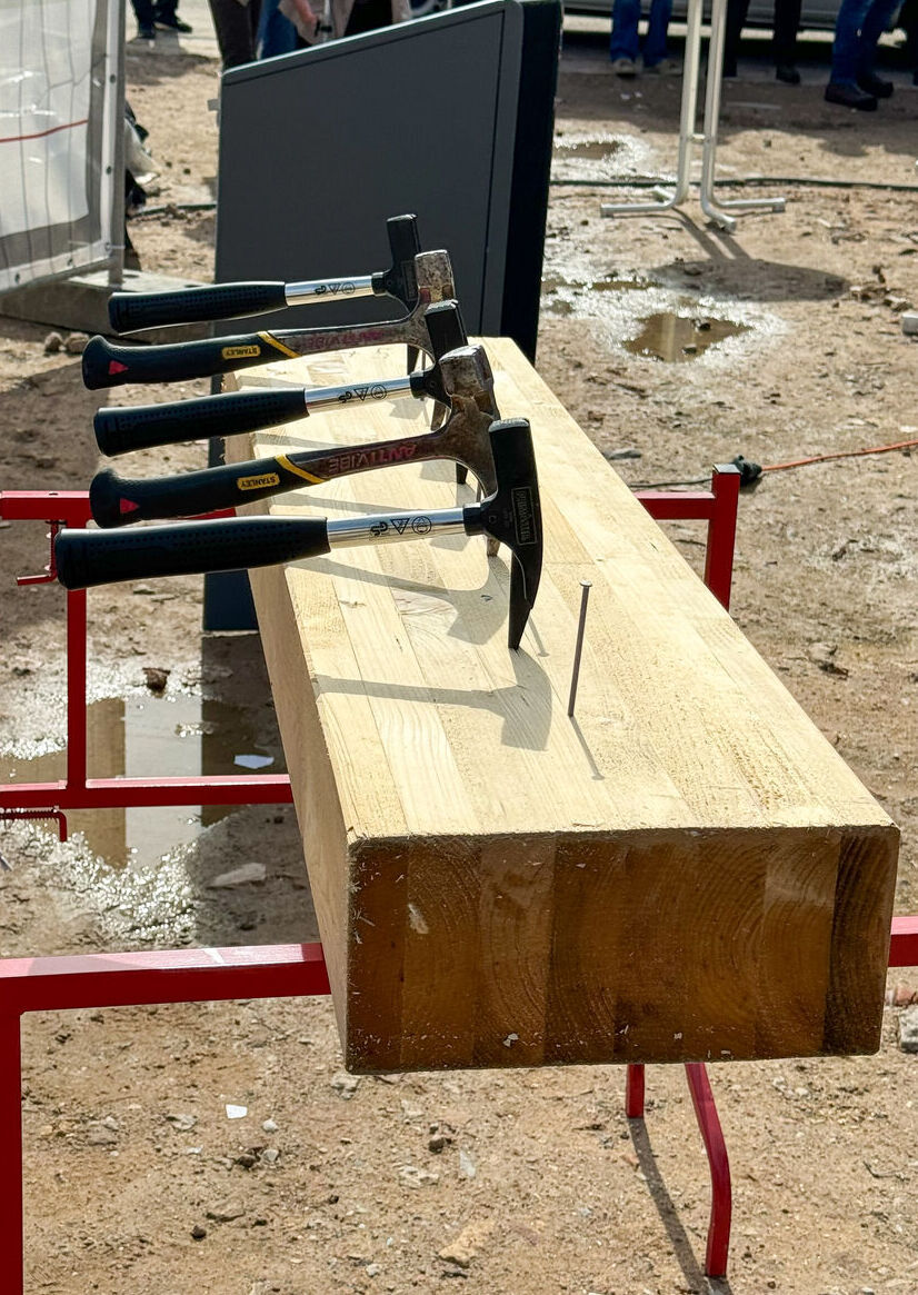 Hammer und Nagel stecken in einem Holzblock welcher auf einer Baustelle steht