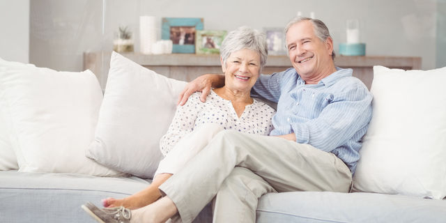  Elderly couple is sitting on a white couch smiling