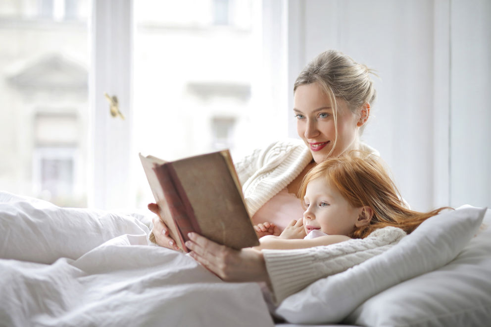 Frau liest ihrer Tochter im Bett ein Buch vor