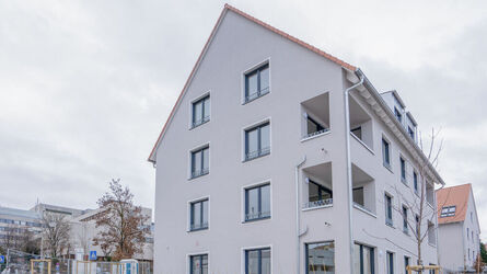 Außenansicht von einem Mehrfamilienhaus, davor steht eine orangene Bank