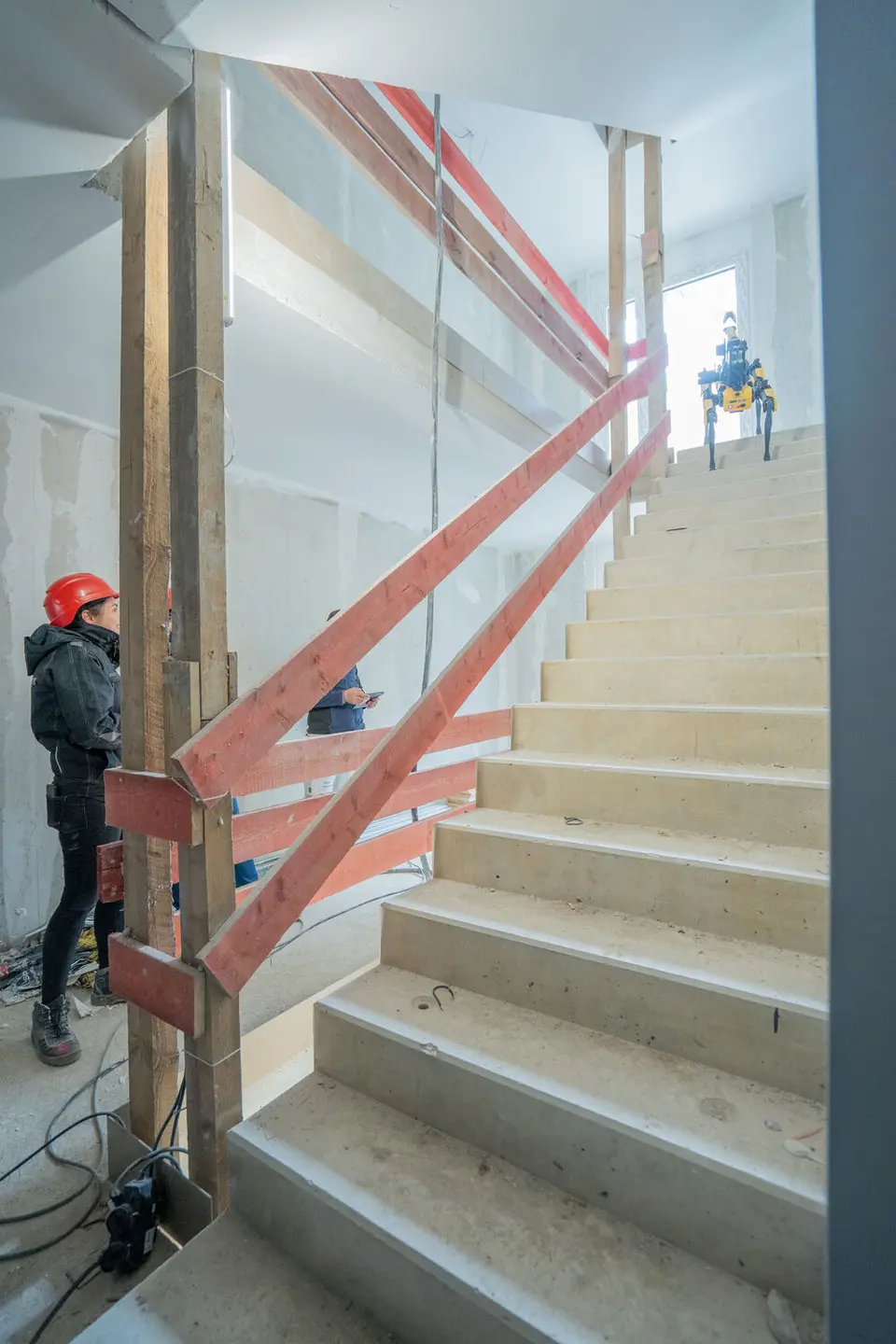 weisenburger Team mit Roboter auf Baustelle im Treppenhaus Baustellenarbeiter und weisenburger-Mitarbeiter testen einen Boston Dynamics Spot Roboter auf einer Treppe