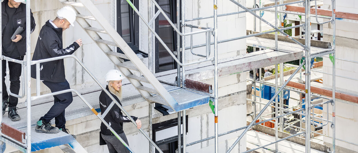 zwei Männer und eine Frau besichtigen eine weisenburger Baustelle und laufen dabei ein Gerüst herunter
