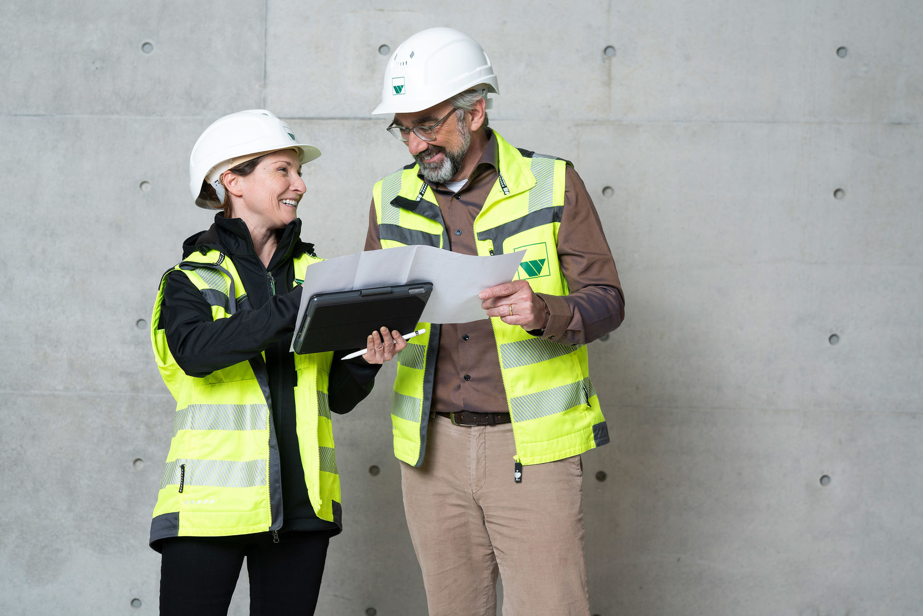 Two employees in construction site clothing discuss a construction plan
