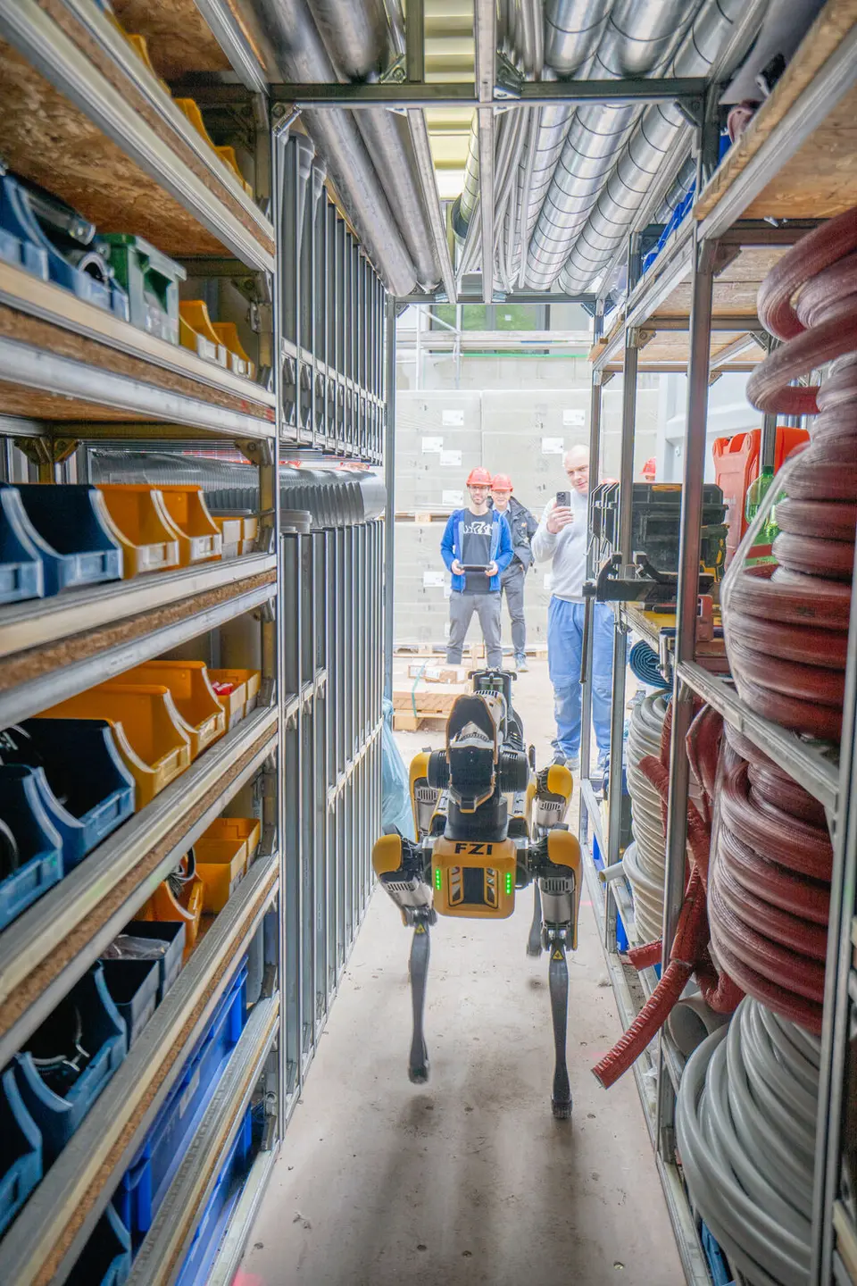 weisenburger Team mit Roboter im Materiallager  Ein Boston Dynamics Spot Roboter läuft durch einen schmalen Gang im Container