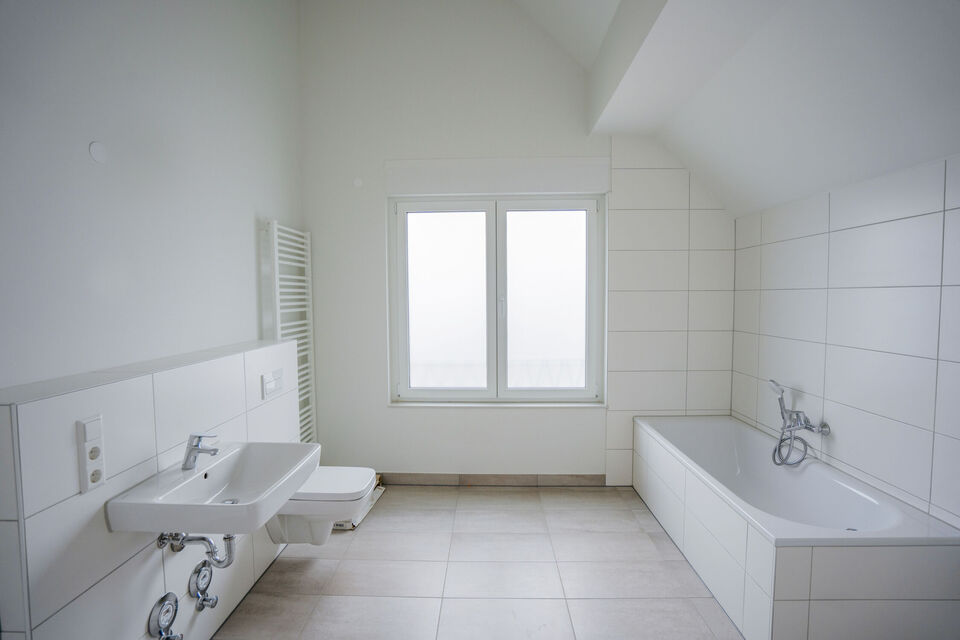 Badezimmer mit weißen Fließen, einer Badewanne, einem Waschbecken und einer Toilette