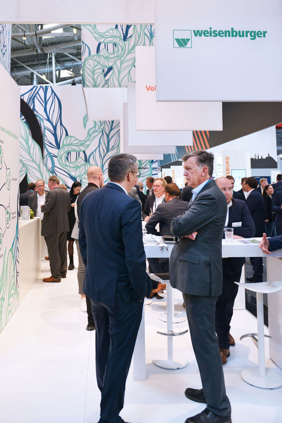 Zwei Männer stehen an dem Stand von weisenburger auf der Expo Real Messe und unterhalten sich