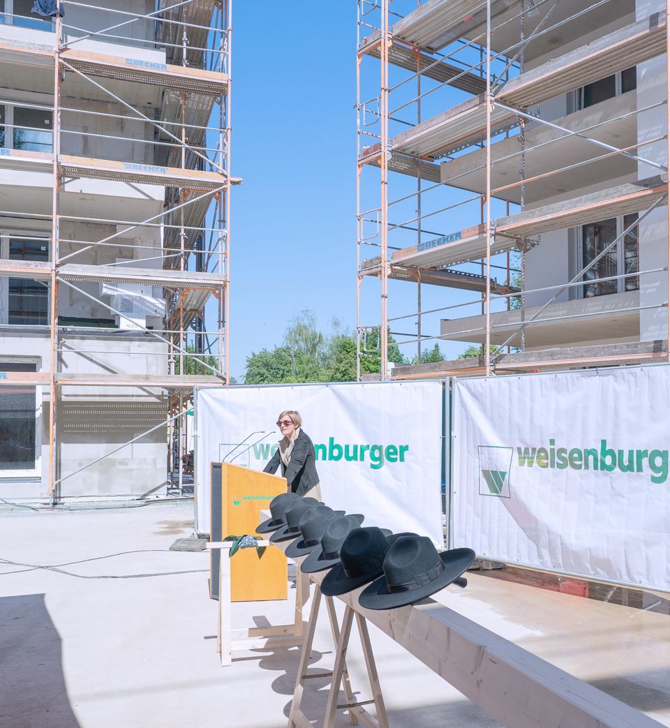 Großbaustelle von mehreren Mehrfamilienhäusern davor stehen Holzstämme mit schwarzen Hüten drauf