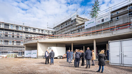 Eine Baustelle mit einem halbfertigen Gebäude und einer Gruppe von Menschen davor.