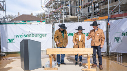 Drei Personen in Handwerkskleidung stehen auf einer Baustelle vor einem Holzbalken mit "weisenburger"-Banner im Hintergrund