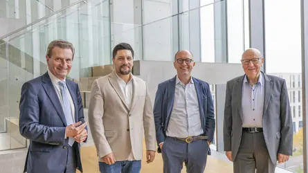 vier Männer in Businesskleidung nebeneinander in einem modernen Gebäude mit Glas- und Beton-Elementen