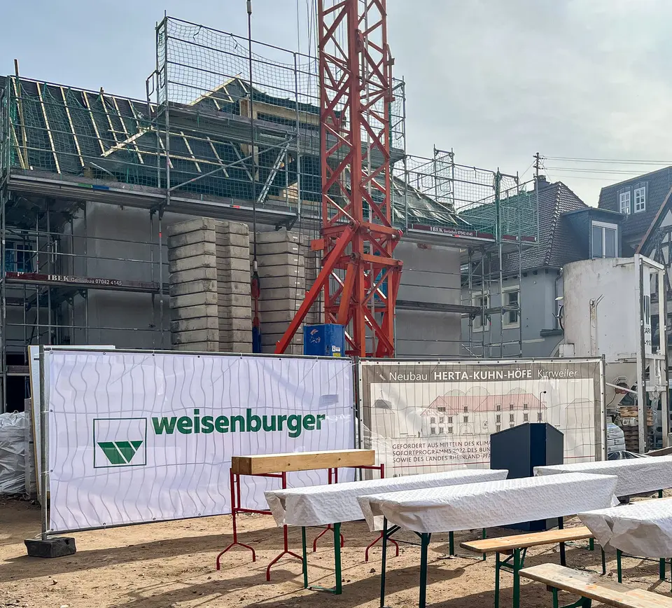 Bänke und Tische stehen auf einer Baustelle vor einem Gebäude, einem Baukran und einem "weisenburger"-Banner