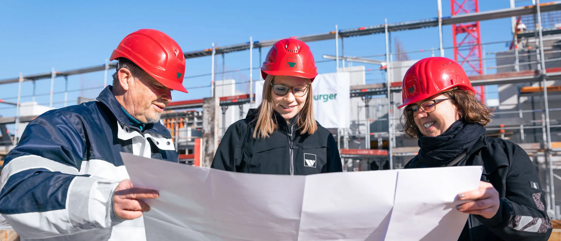 weisenburger-bau-Planung drei Bauleiter der Firma weisenburger stehen auf einer Baustelle und studieren einen Bauplan