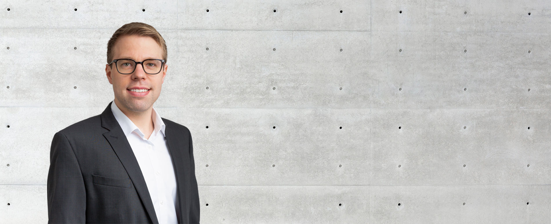A man in front of a concrete wall looks at the camera