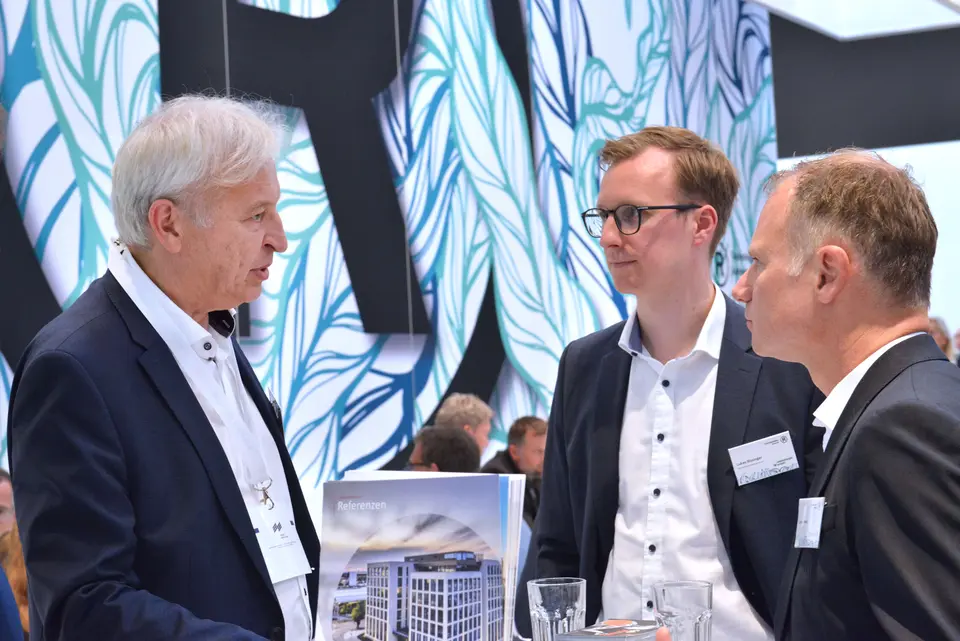 Drei Männer stehen an dem Stand von weisenburger auf der Expo Real Messe und unterhalten sich