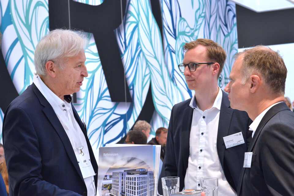 Drei Männer stehen an dem Stand von weisenburger auf der Expo Real Messe und unterhalten sich