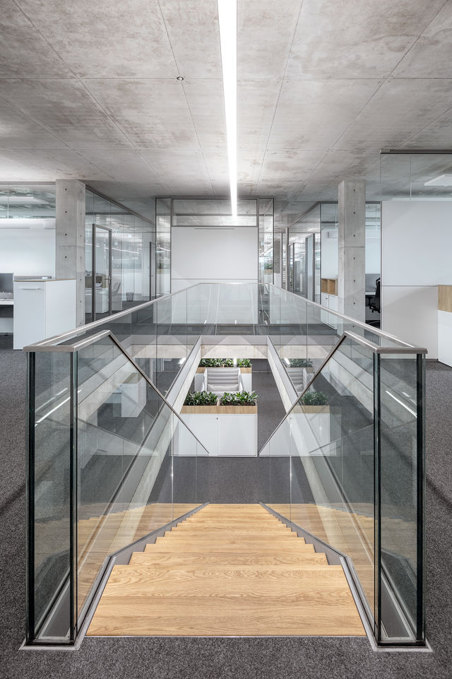 View of a wooden staircase with a glass railing that leads down one floor