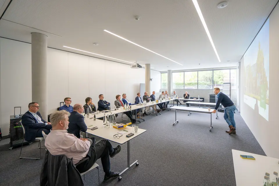 Mehrere Männer sitzen in einem Besprechungsraum und hören bei einem Vortrag zu