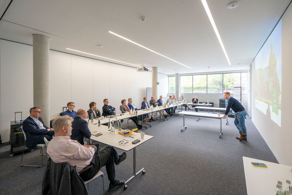 Mehrere Männer sitzen in einem Besprechungsraum und hören bei einem Vortrag zu