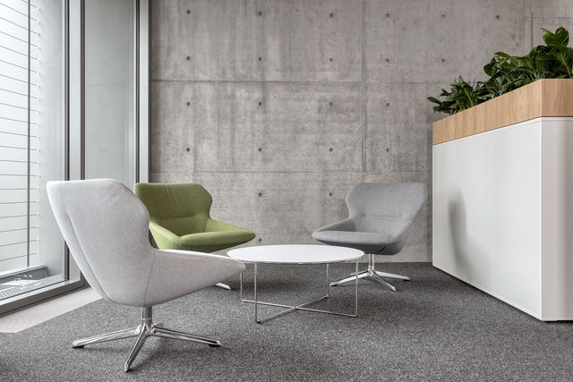 Three comfortable chairs stand around a low white table in front of an exposed concrete wall