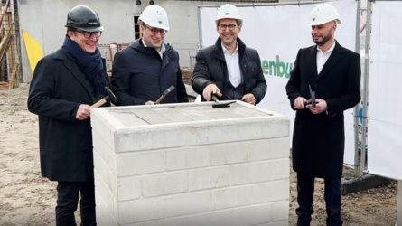 Vier Männer mit Bauhelmen stehen auf einer Baustelle und halten Hammer in der Hand, während sie an einer Grundsteinlegung teilnehmen