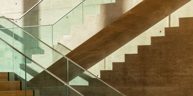 Die frei tragende Betontreppe im Foyer wird vom Sonnenlicht angestrahlt und wirft Schatten.