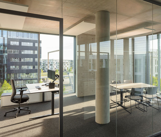 View through glass partitions into a light-flooded office with a desk and conference table.