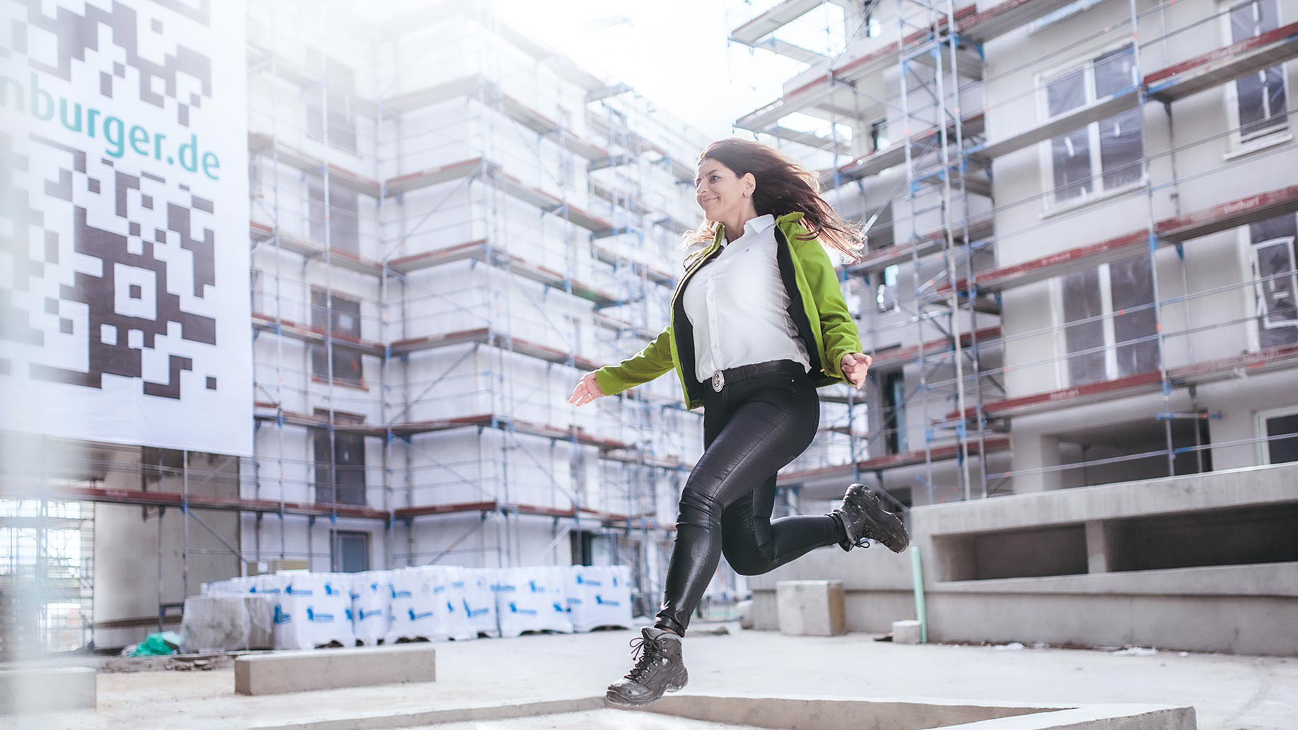 A woman is jumping into the air in front of a construction site